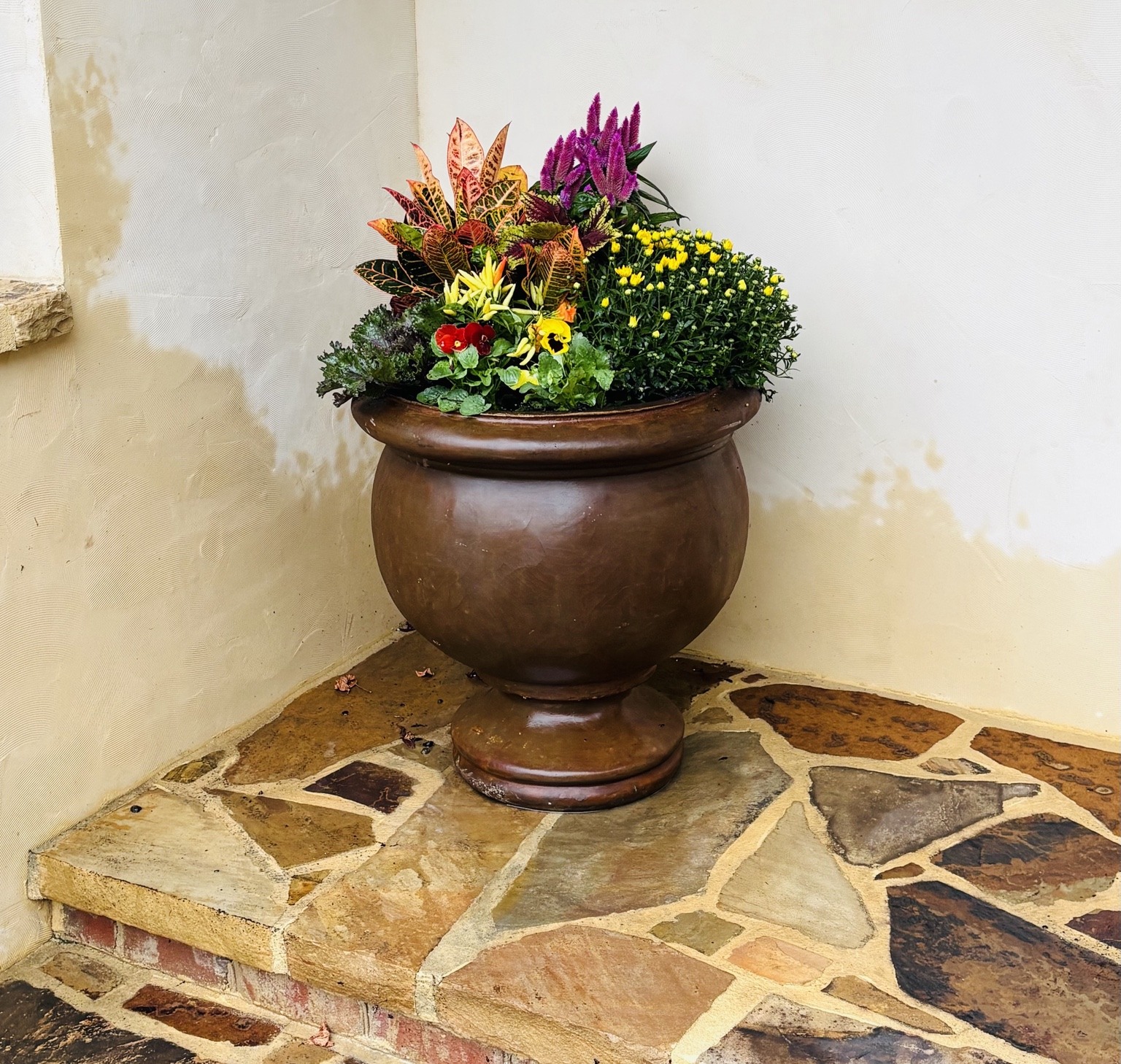 Brown urn with fall flowers on a stone porch