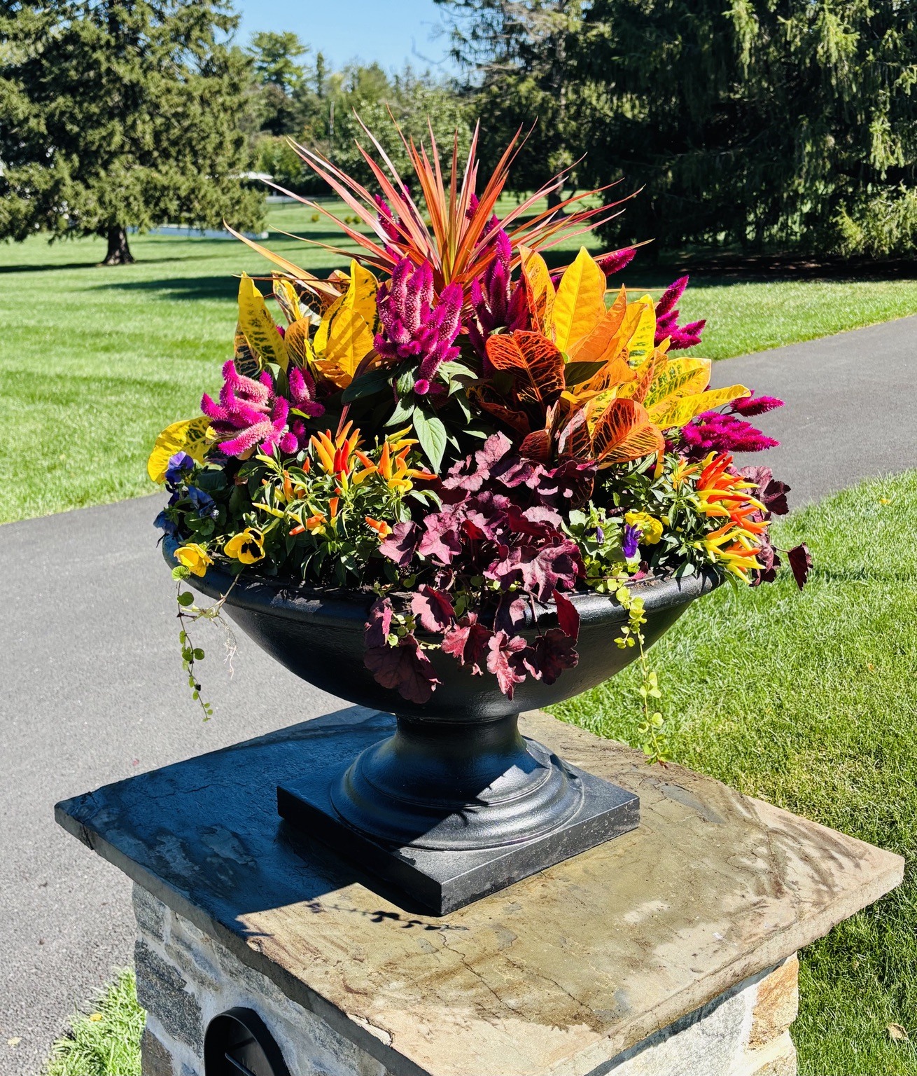 Vibrant fall urn on a stone pedestal in the garden