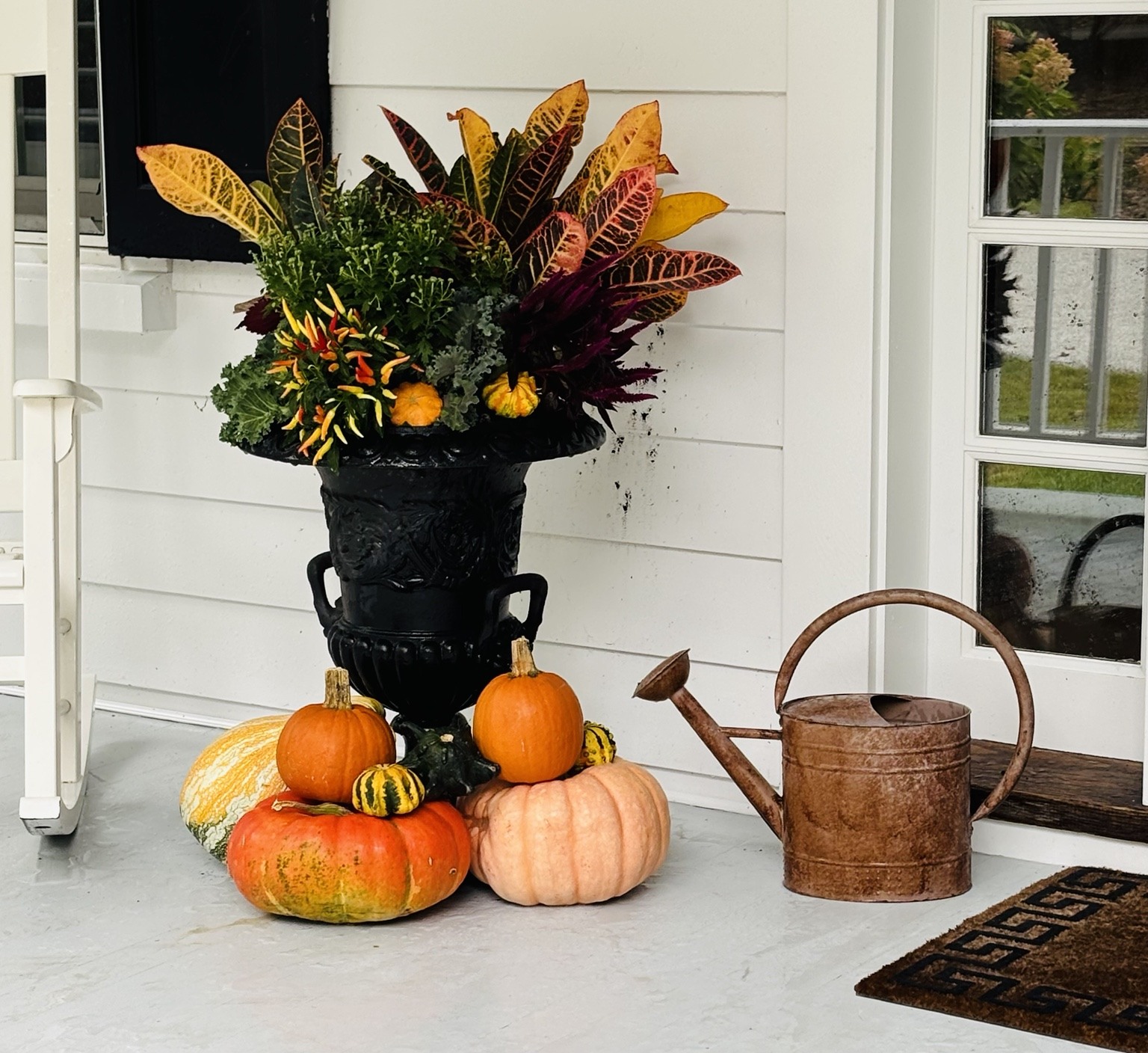 Black fall urn styled with colorful foliage, pumpkins, and gourds