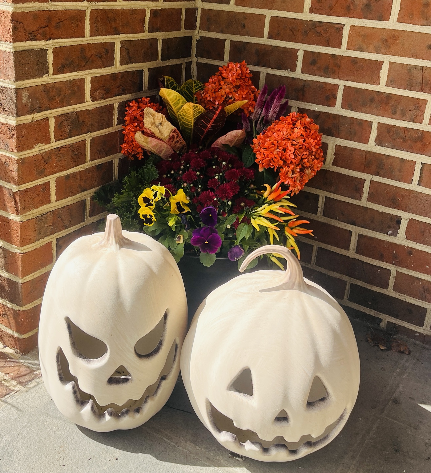 Fall planter with orange flowers, ornamental peppers, pansies, and white pumpkins on a brick porch