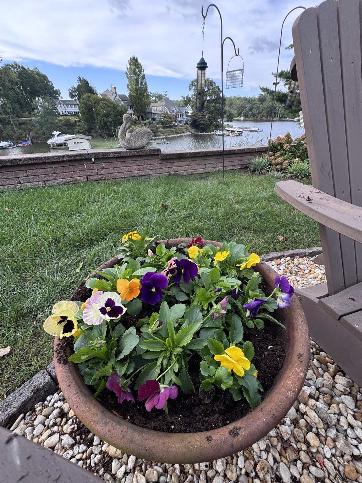 Terracotta bowl of yellow, purple, and white pansies beside a lakeside patio