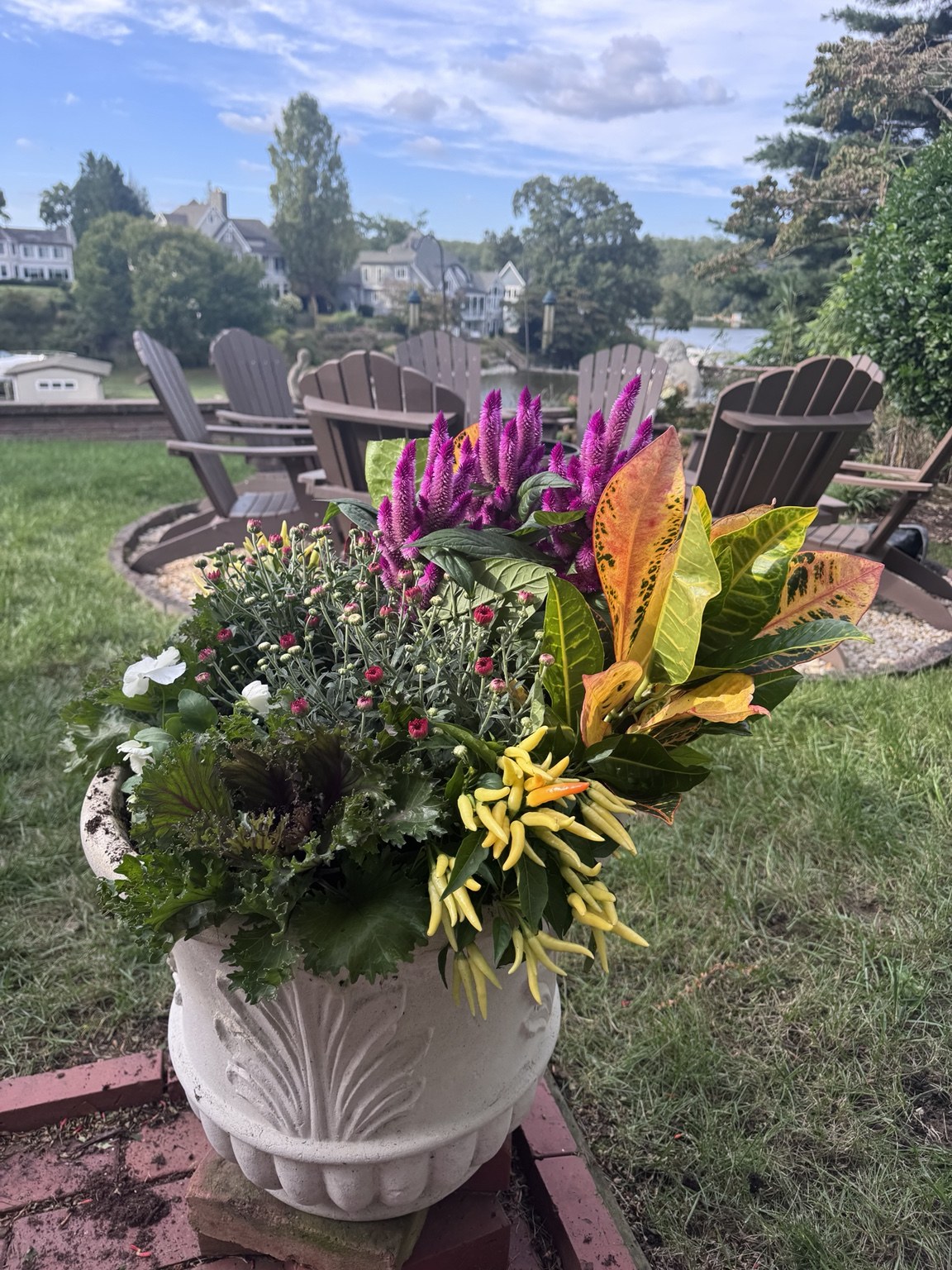 Ornamental white urn with purple celosia, ornamental peppers, and fall foliage on a lakeside patio