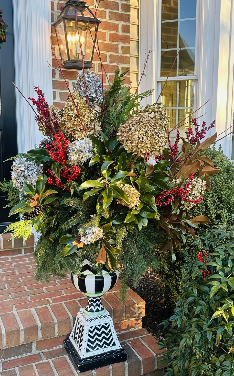 Festive evergreen container with berries beside a brick entry