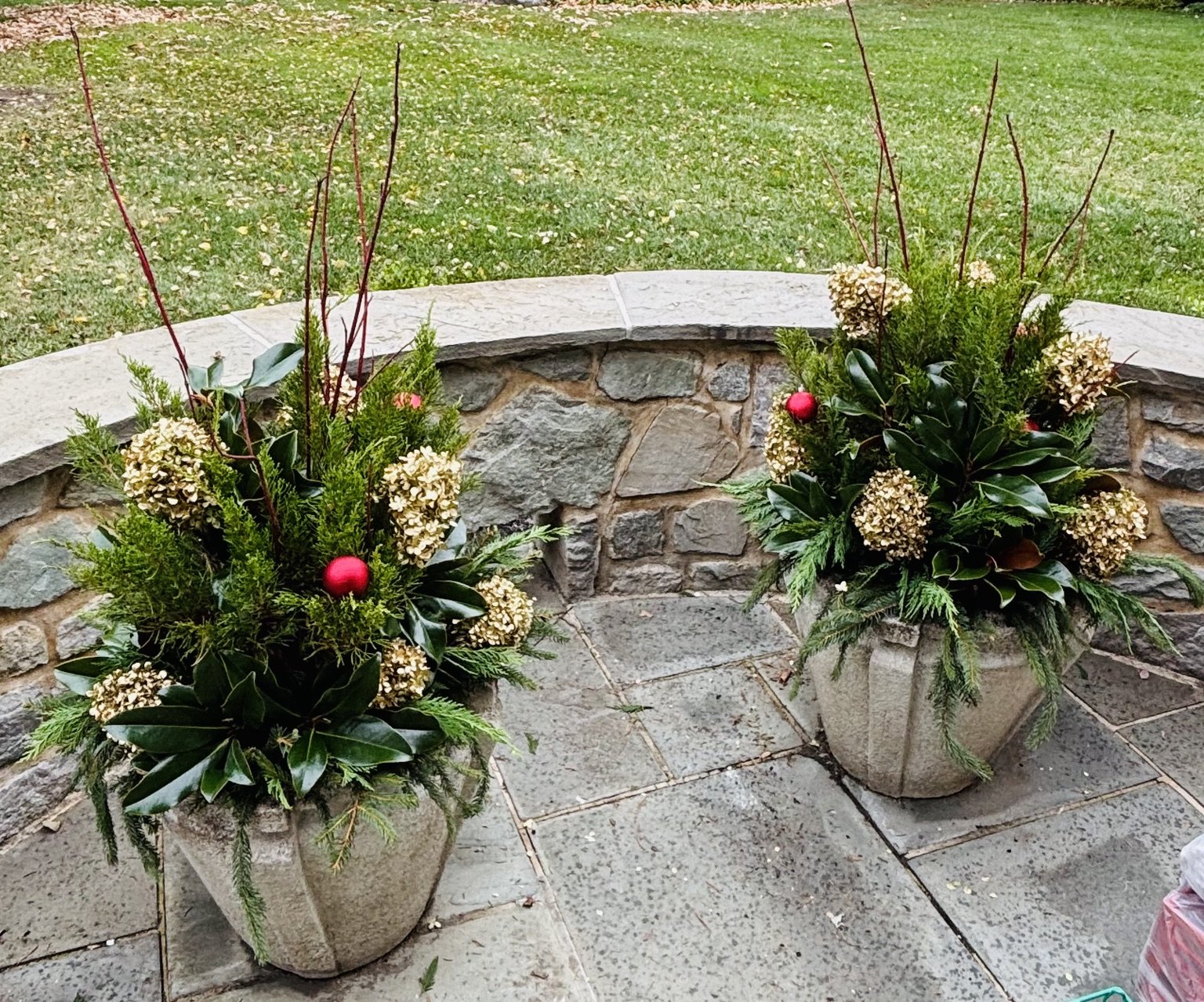 Pair of holiday containers with evergreen branches and red accents on a stone terrace