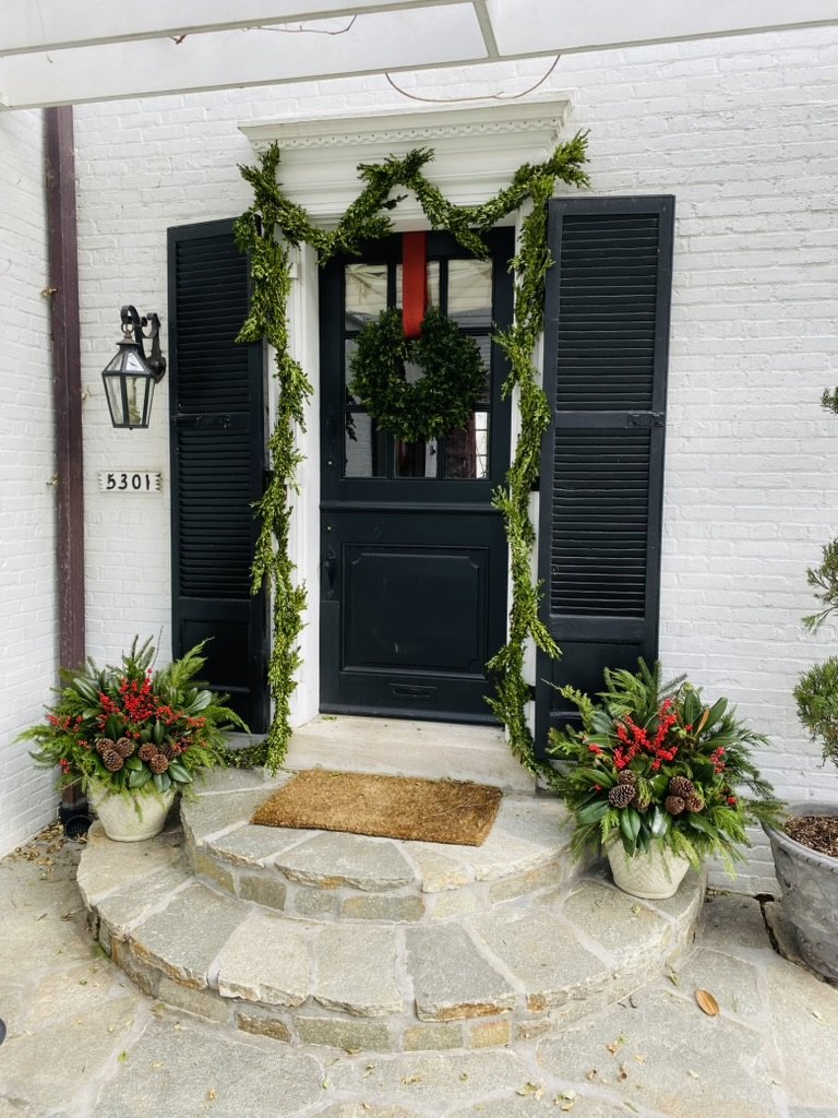 White front entrance framed with holiday garland, a wreath, and seasonal planters