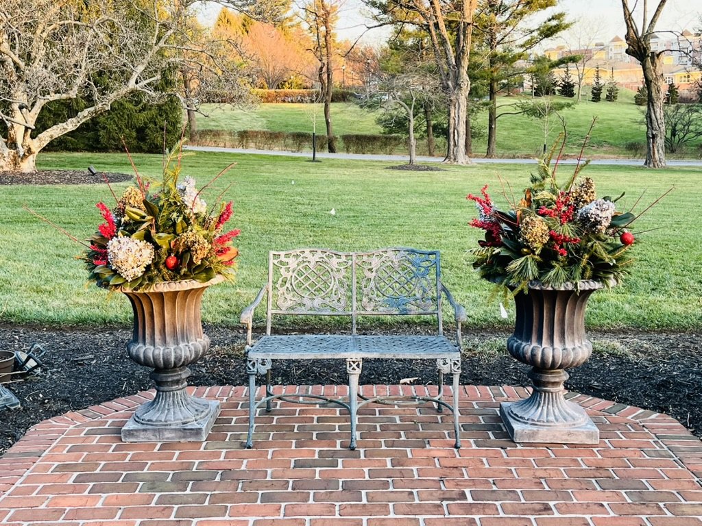 Pair of decorative holiday urns on a brick terrace overlooking a garden