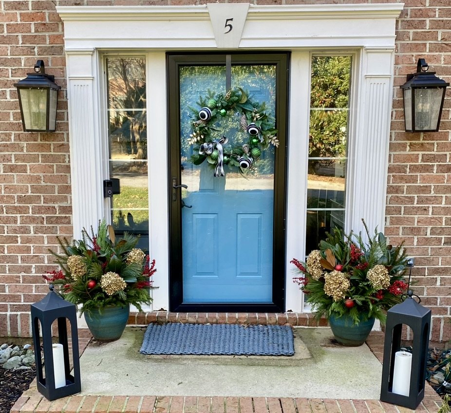Blue front door framed by matching seasonal planters and lanterns