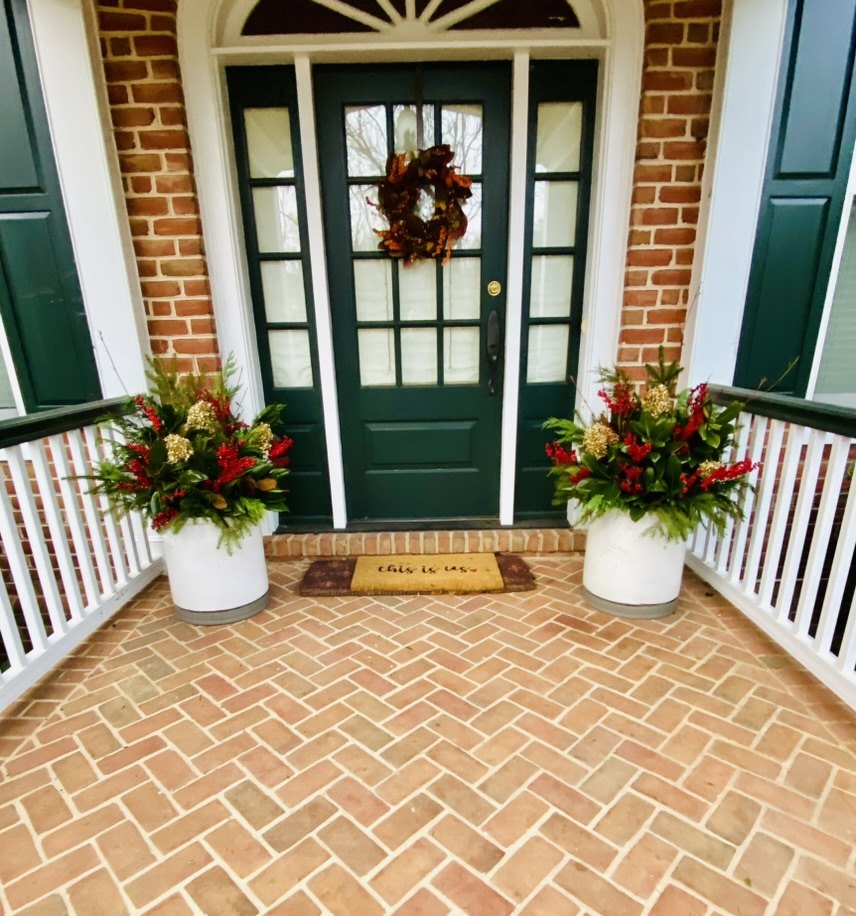 Pair of white holiday planters on a covered brick porch