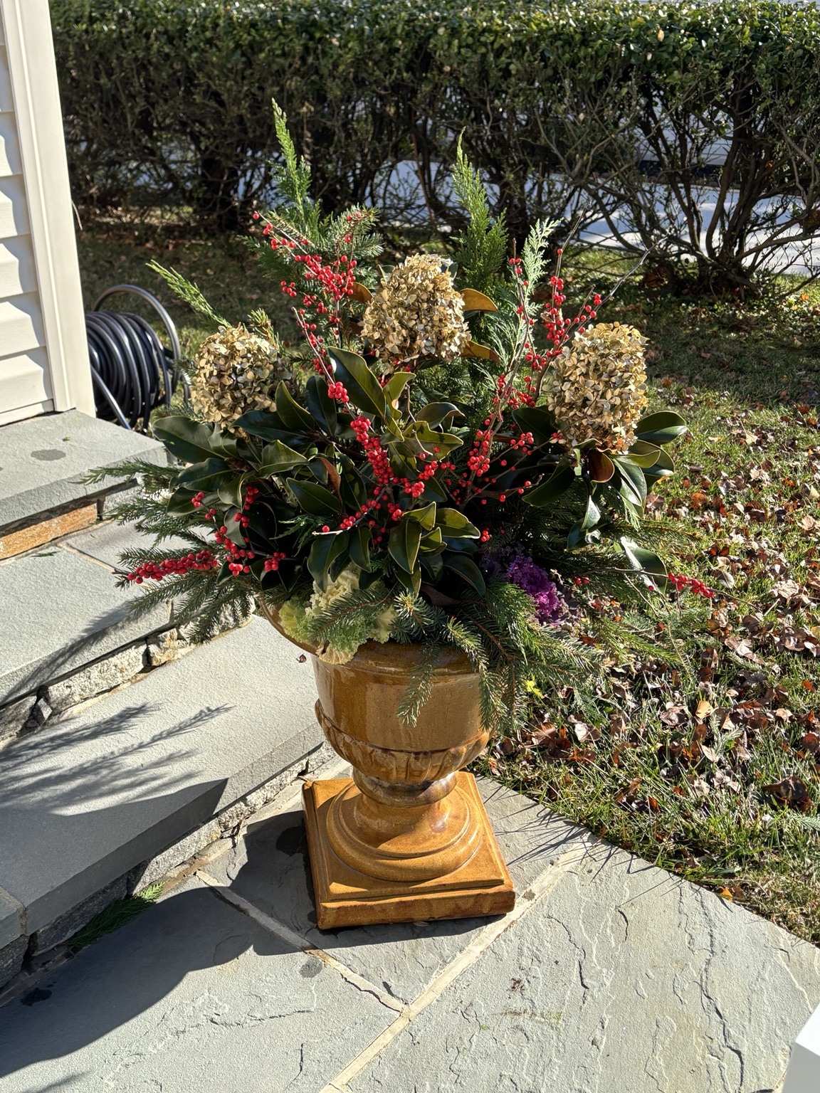 Evergreen holiday arrangement in a decorative urn beside a patio