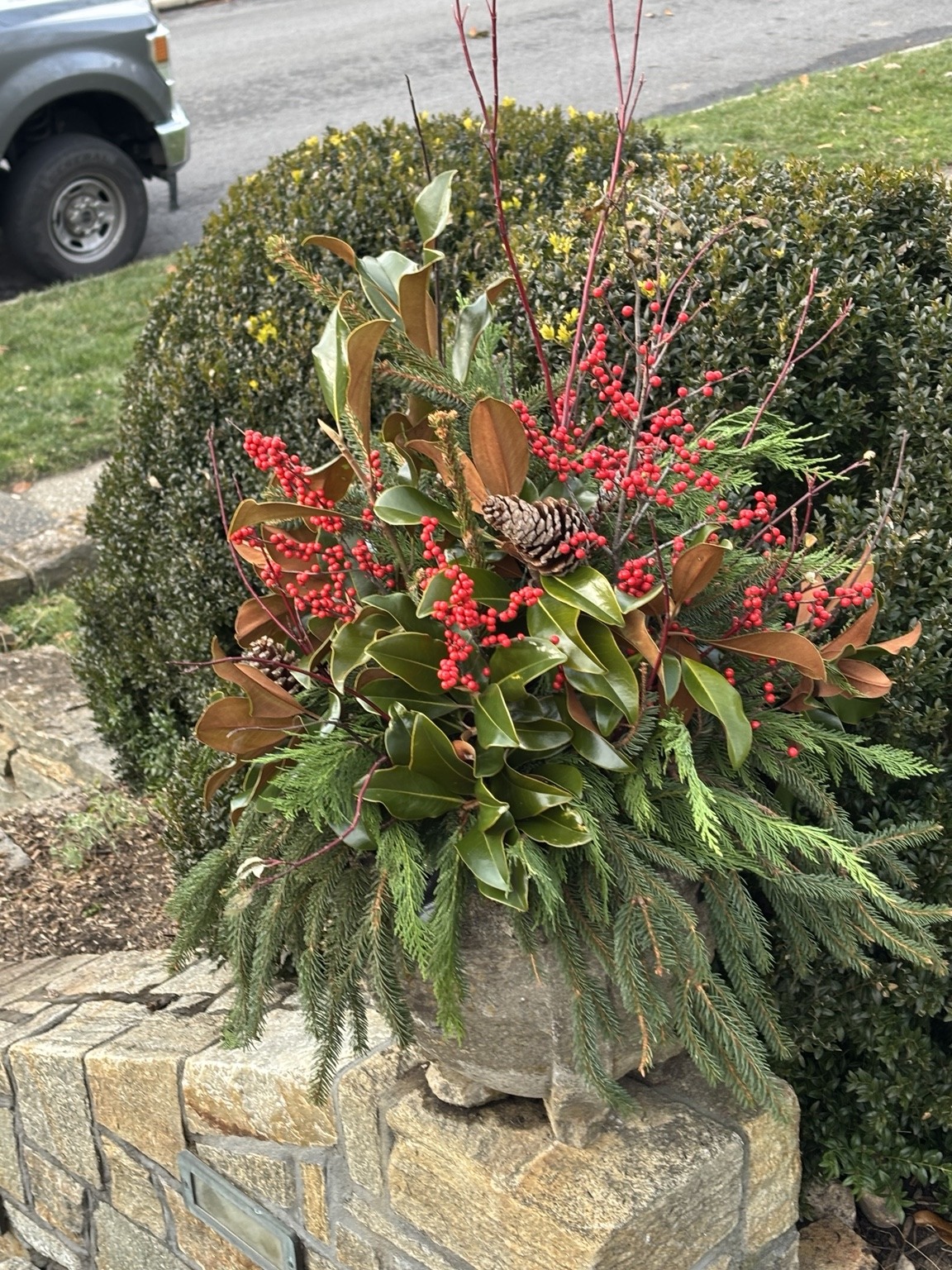 Holiday urn filled with evergreen branches on a stone garden pillar