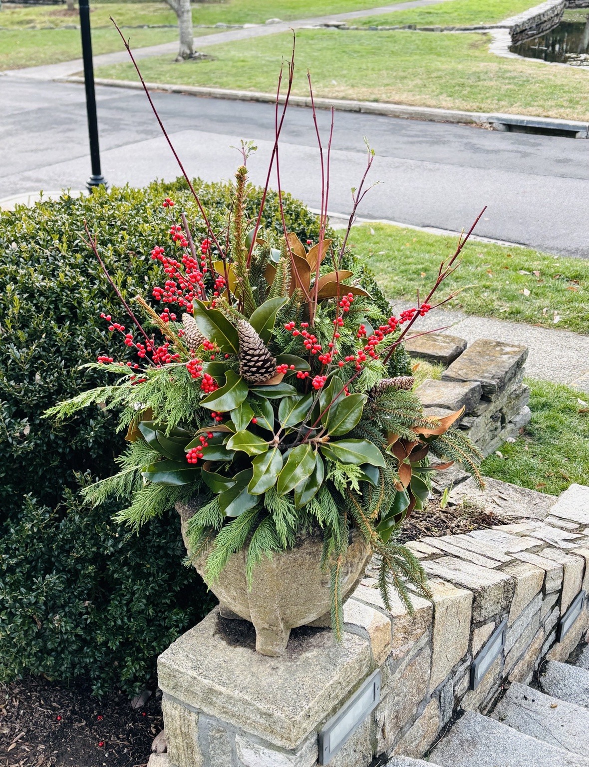 Evergreen arrangement with berries beside a stone garden wall