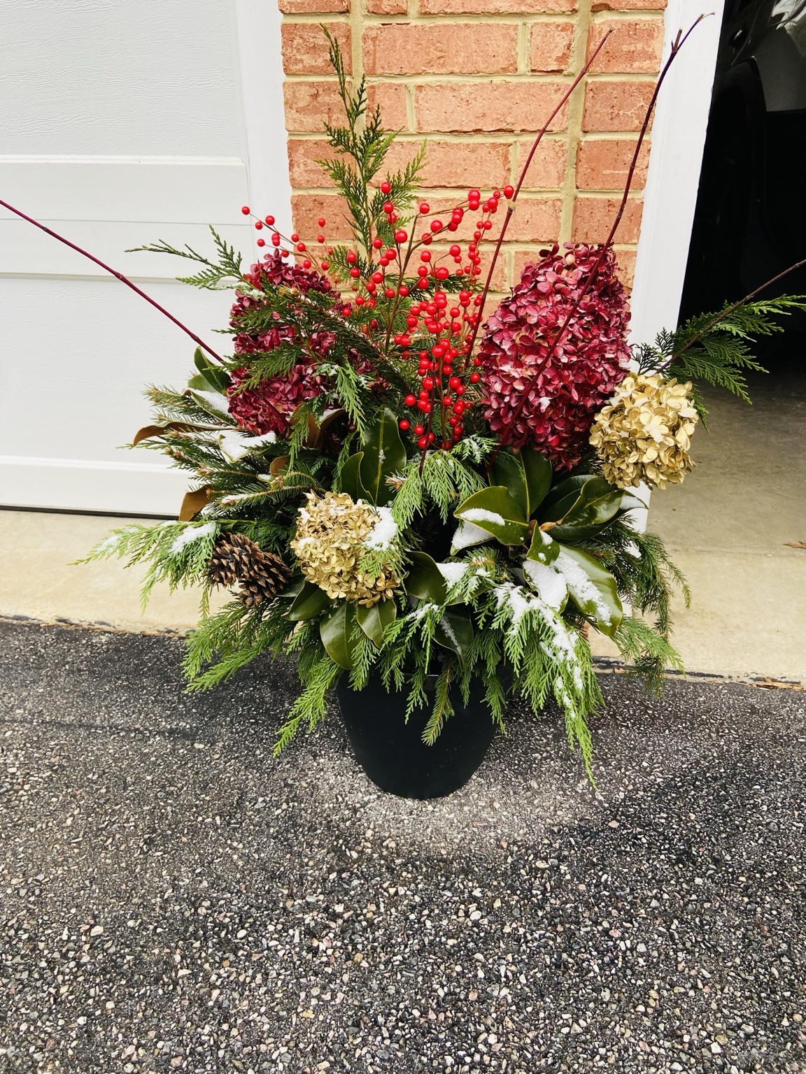 Red and evergreen holiday arrangement beside a brick entry