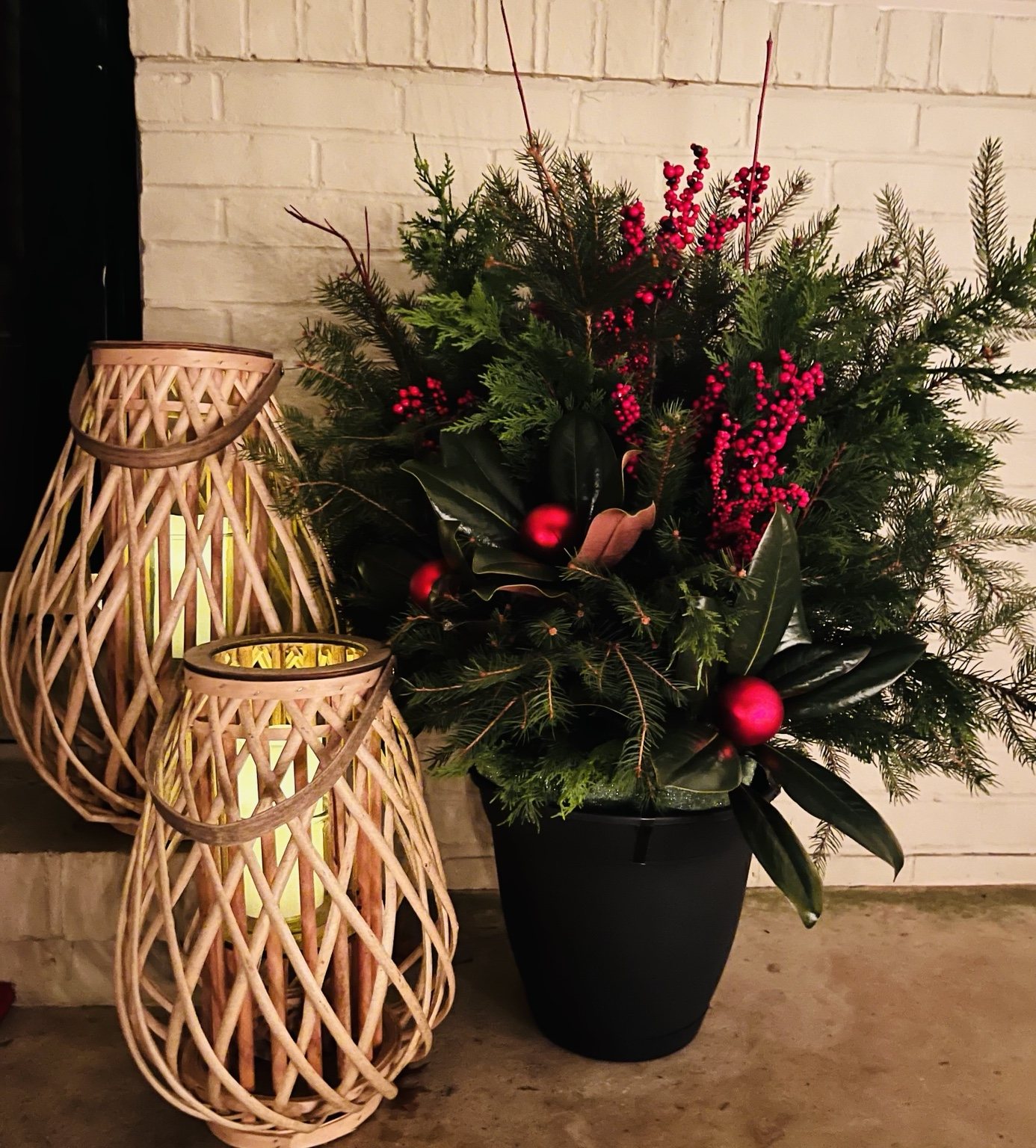 Evergreen holiday planter with berries beside decorative lanterns