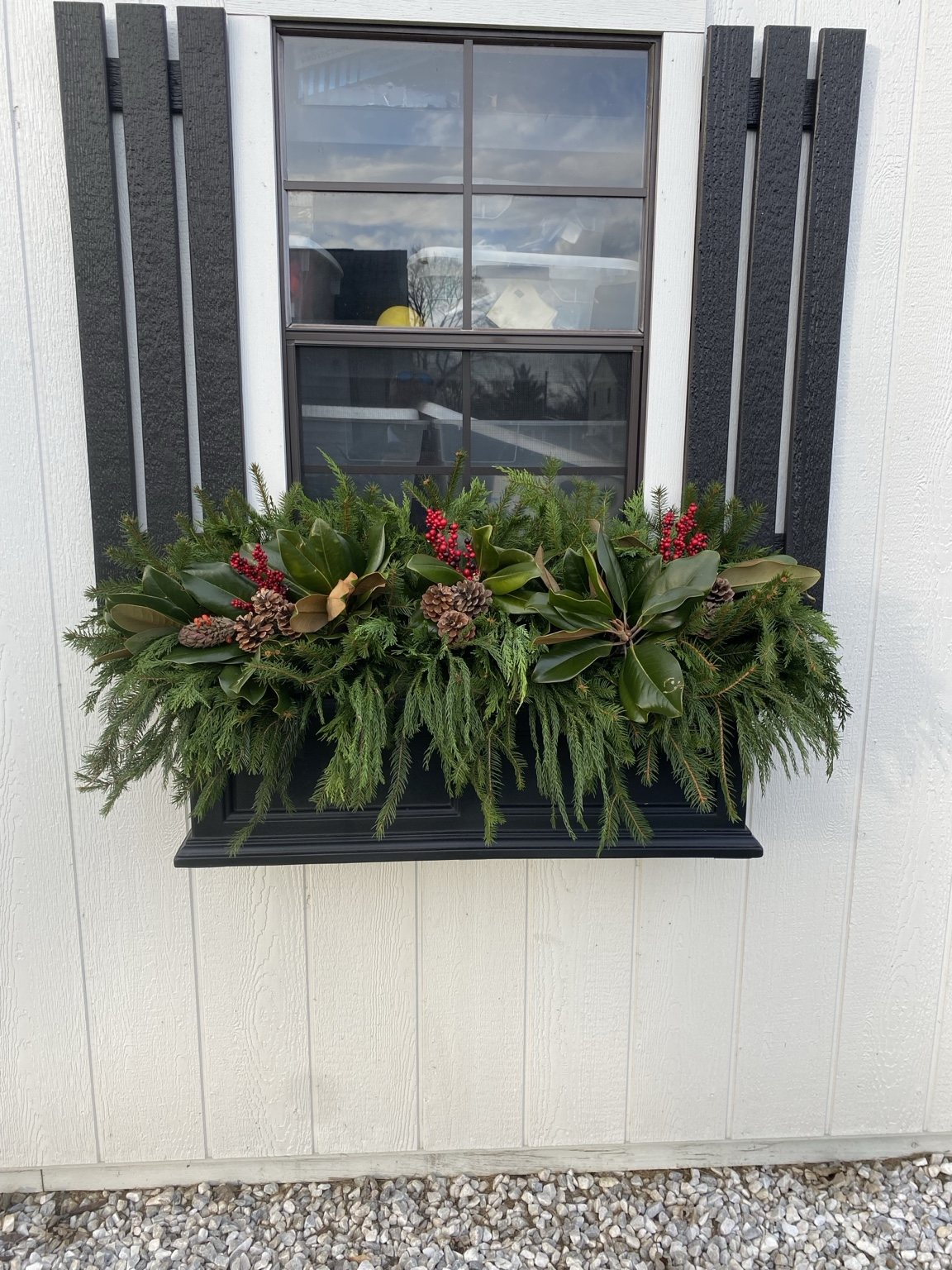 Holiday window box filled with evergreen branches and red accents