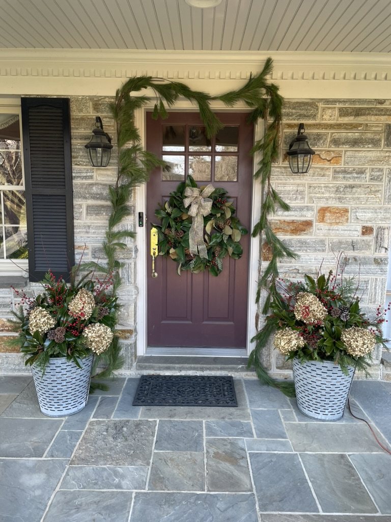 Holiday wreath and matching evergreen planters at a stone front entrance
