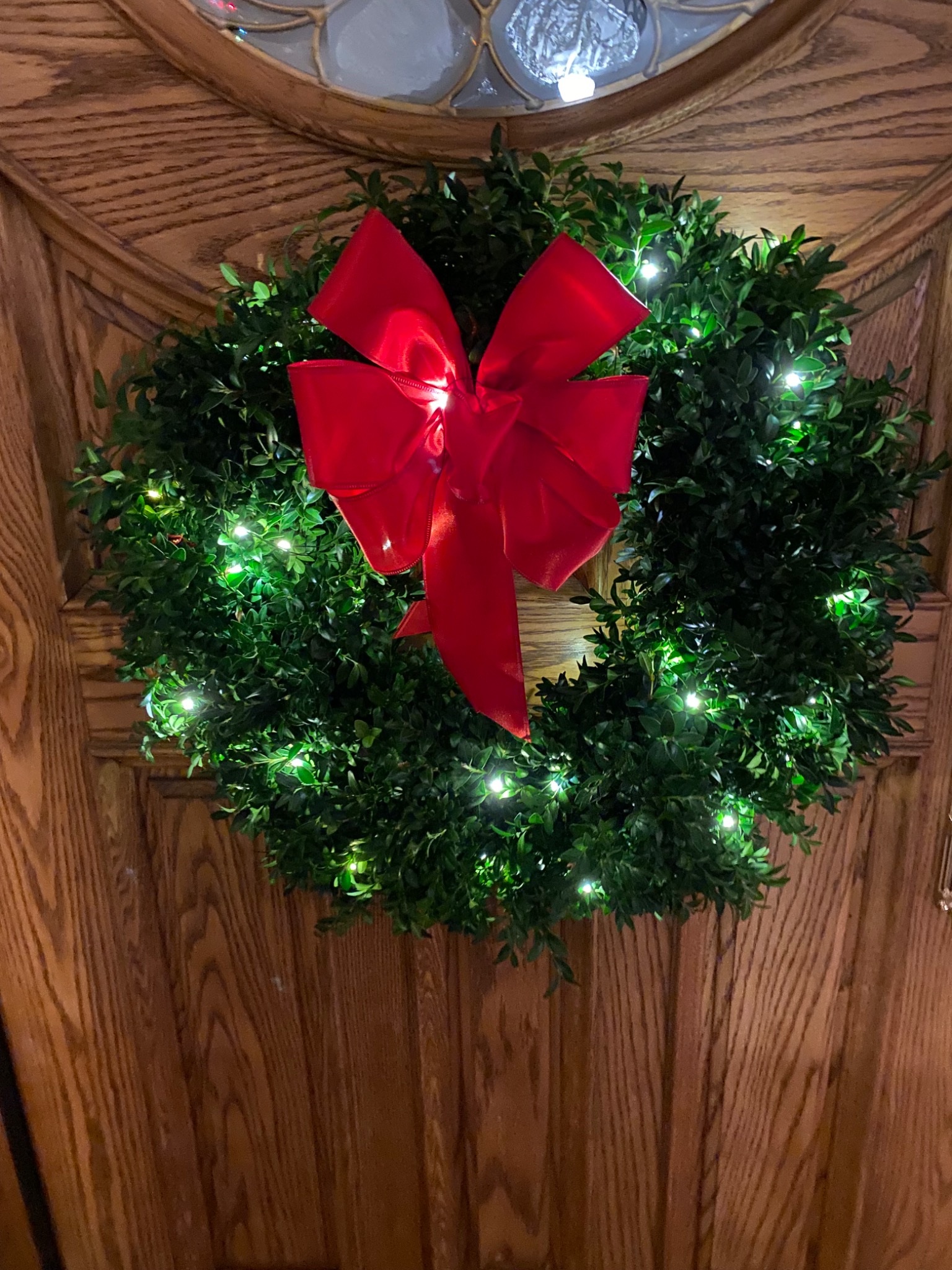 Lit evergreen wreath with a bright red bow on a wooden door