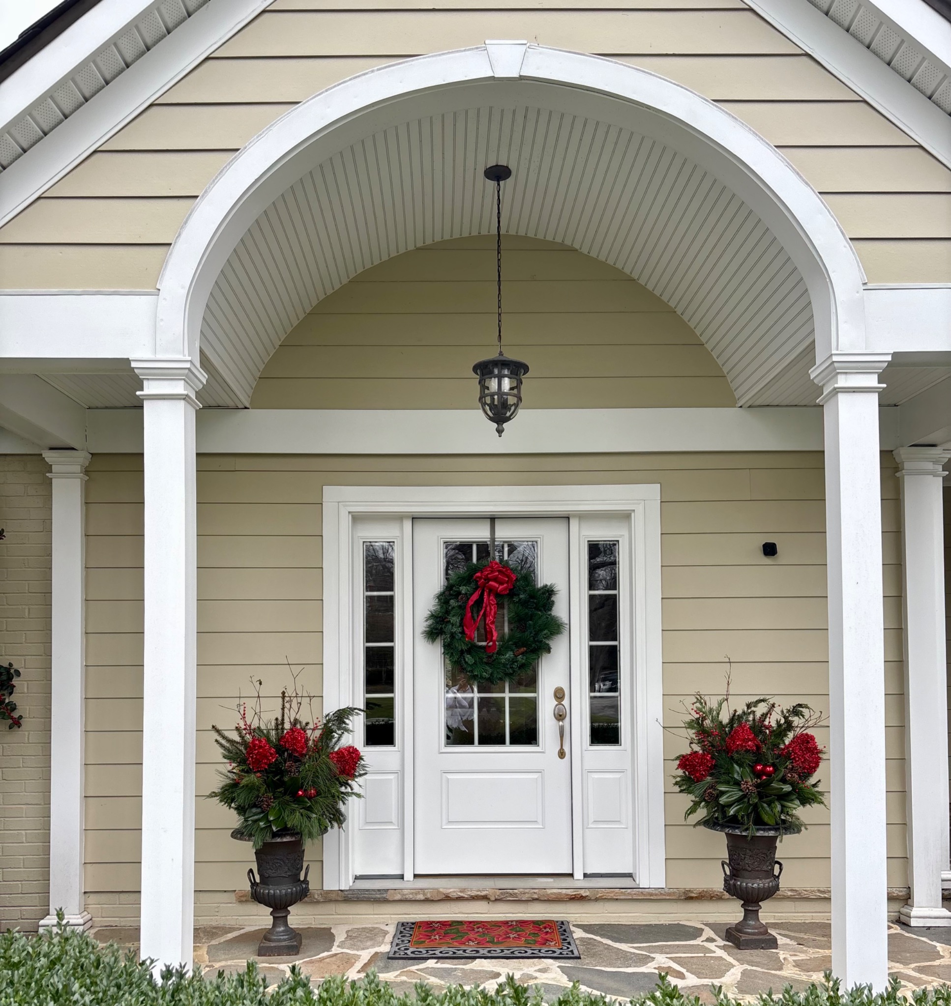Matching holiday urns beneath a white arched entry with a wreath on the door