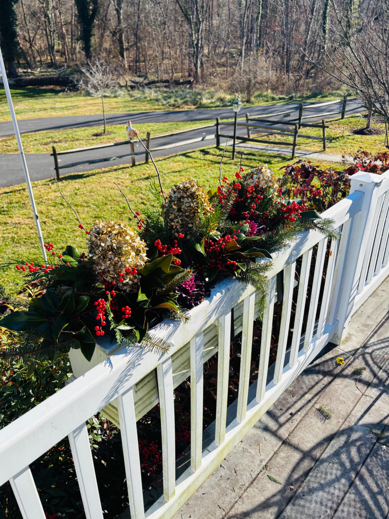 Holiday planter along a white porch railing, filled with evergreens, berries, and seasonal accents