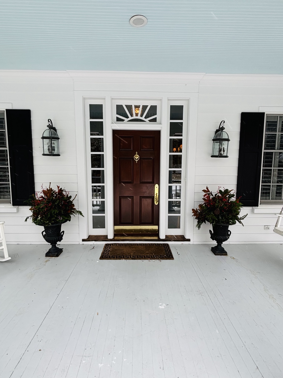 Matching dark urns filled with evergreen, red berries, and pinecones flanking a white front door