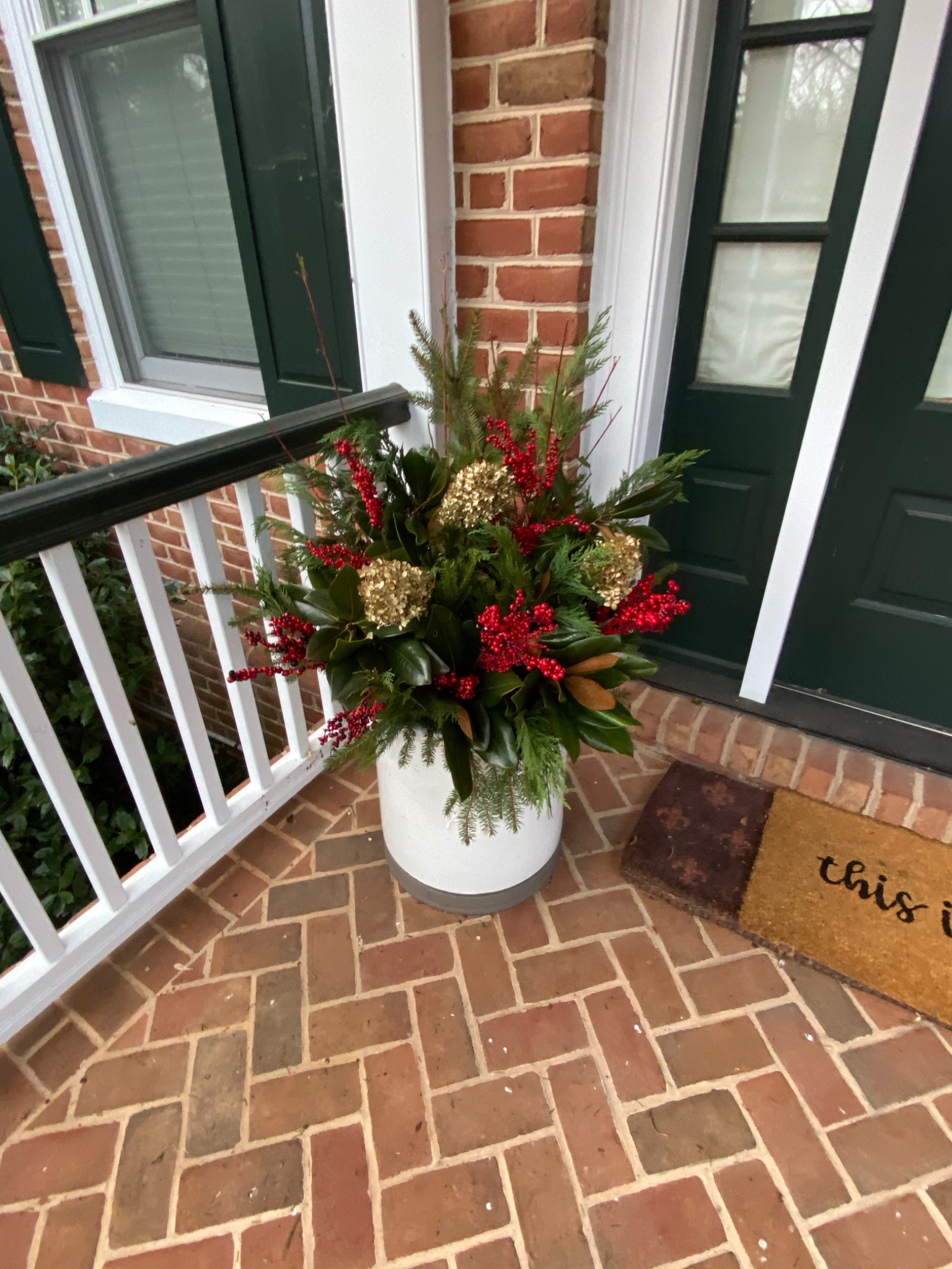Holiday planter with evergreens, red berries, and hydrangeas beside a dark green front door