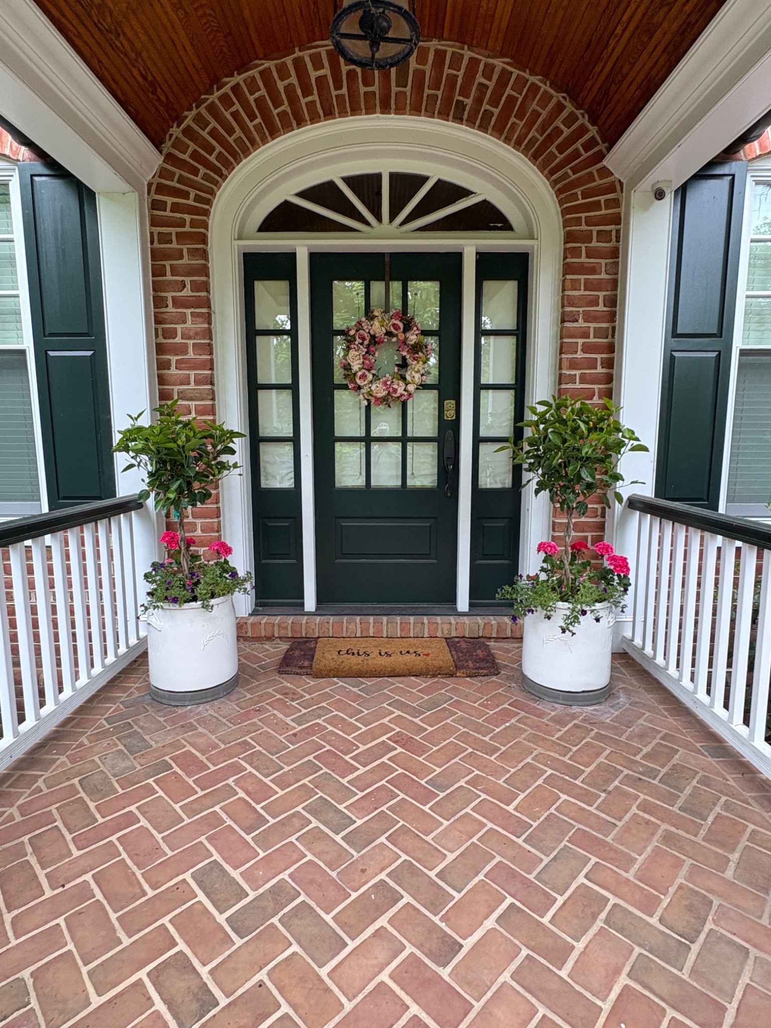 Pair of white porch planters with pink flowers flanking a dark green front door