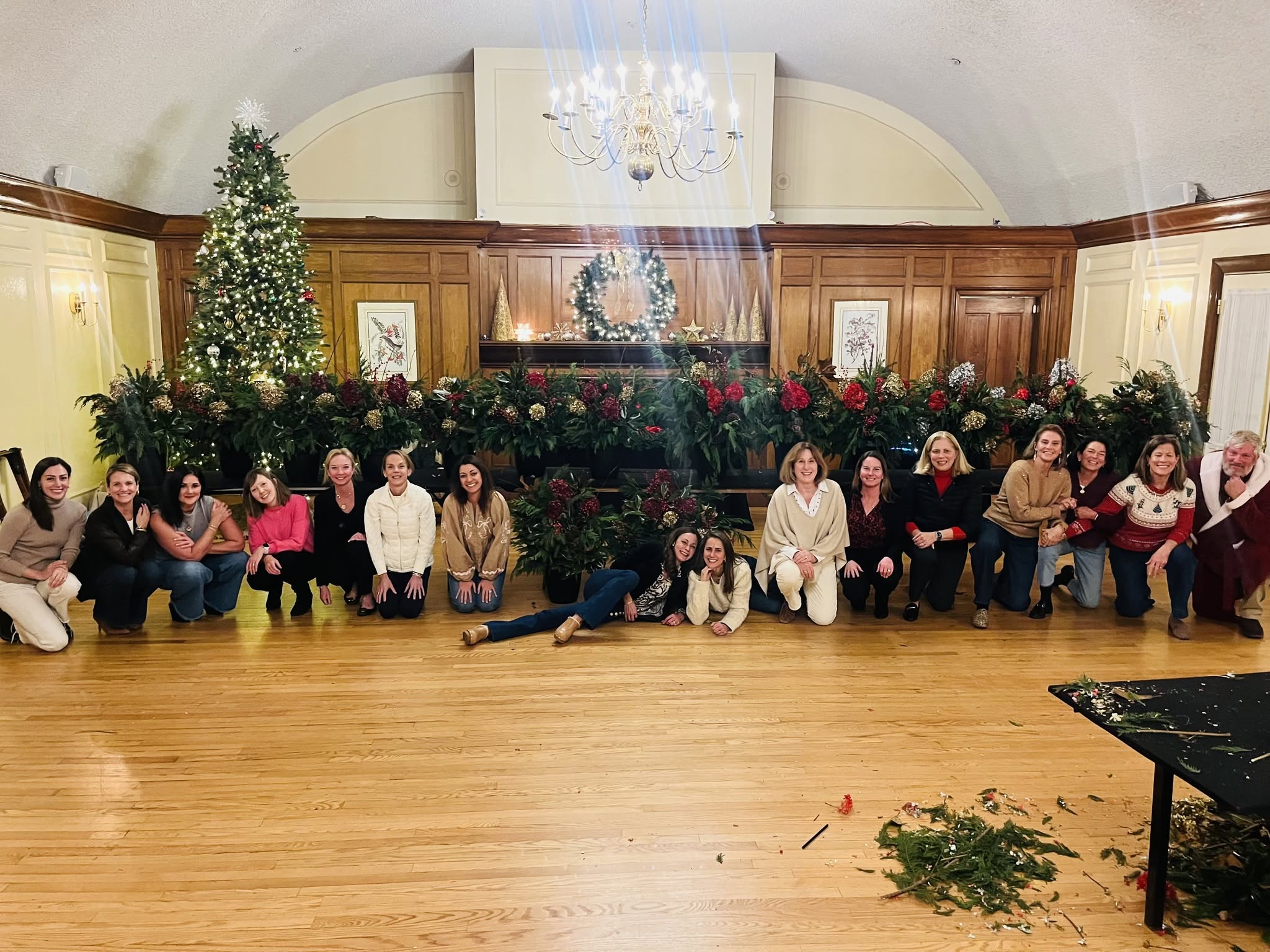 Holiday workshop guests gathered in front of a long display of festive evergreen arrangements