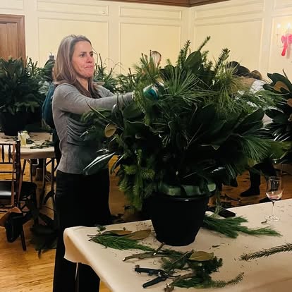 Guest arranging evergreen branches and magnolia in a holiday planter at a workshop