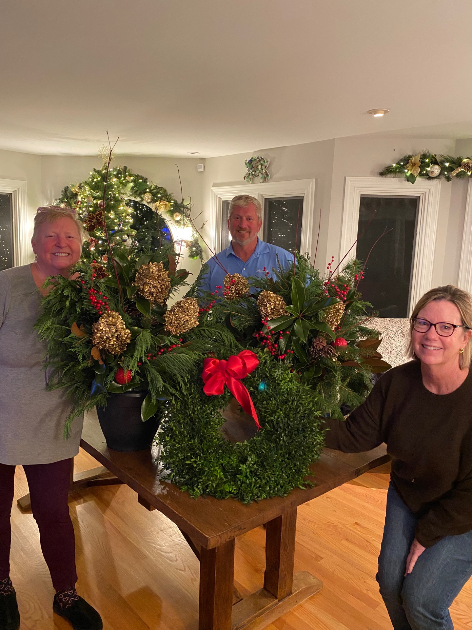 Three guests with finished evergreen holiday arrangements and a boxwood wreath at a workshop
