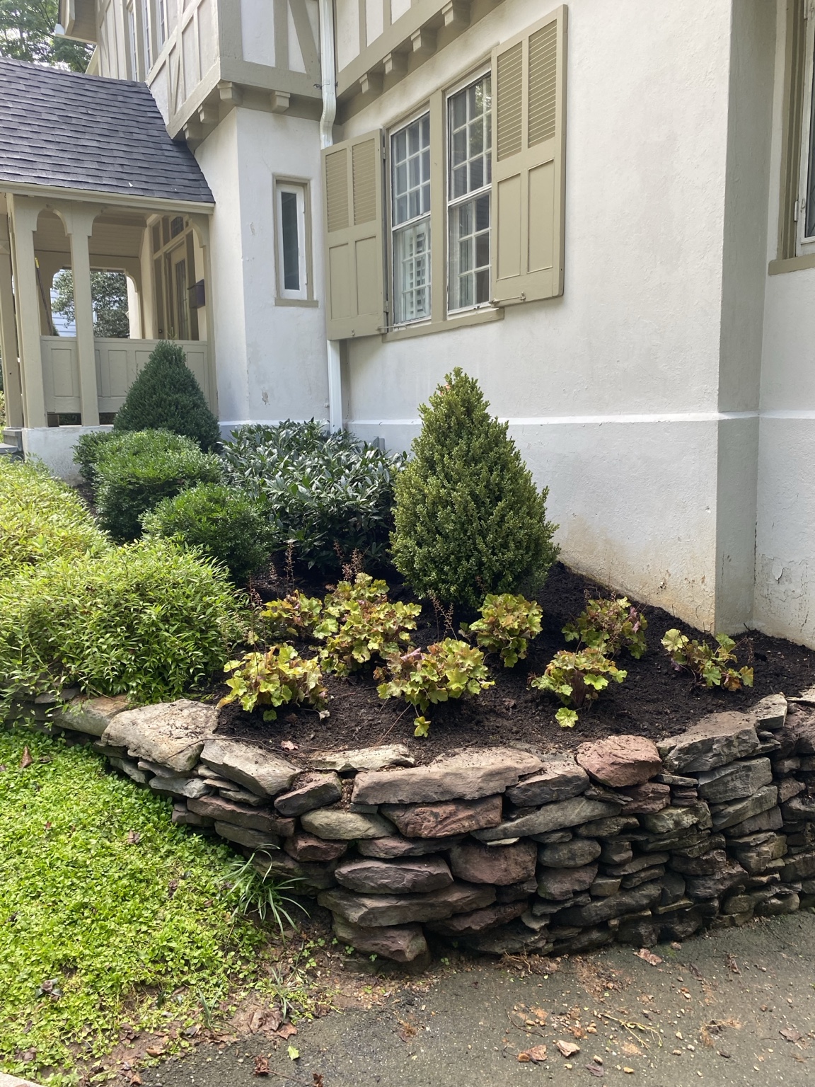 Layered foundation planting with evergreen shrubs and colorful foliage above a natural stone retaining wall