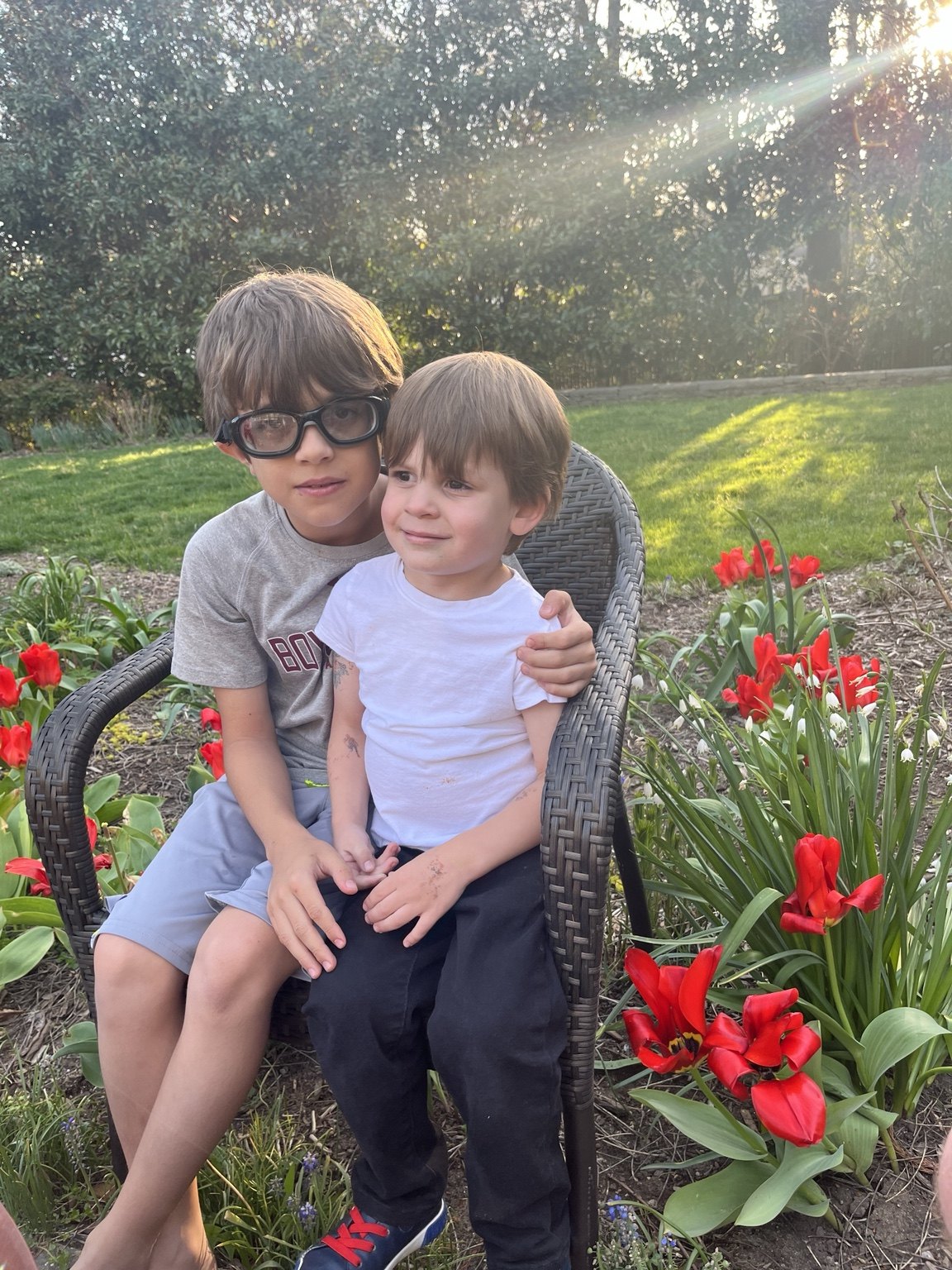 Two boys sitting together among blooming red tulips in a spring garden