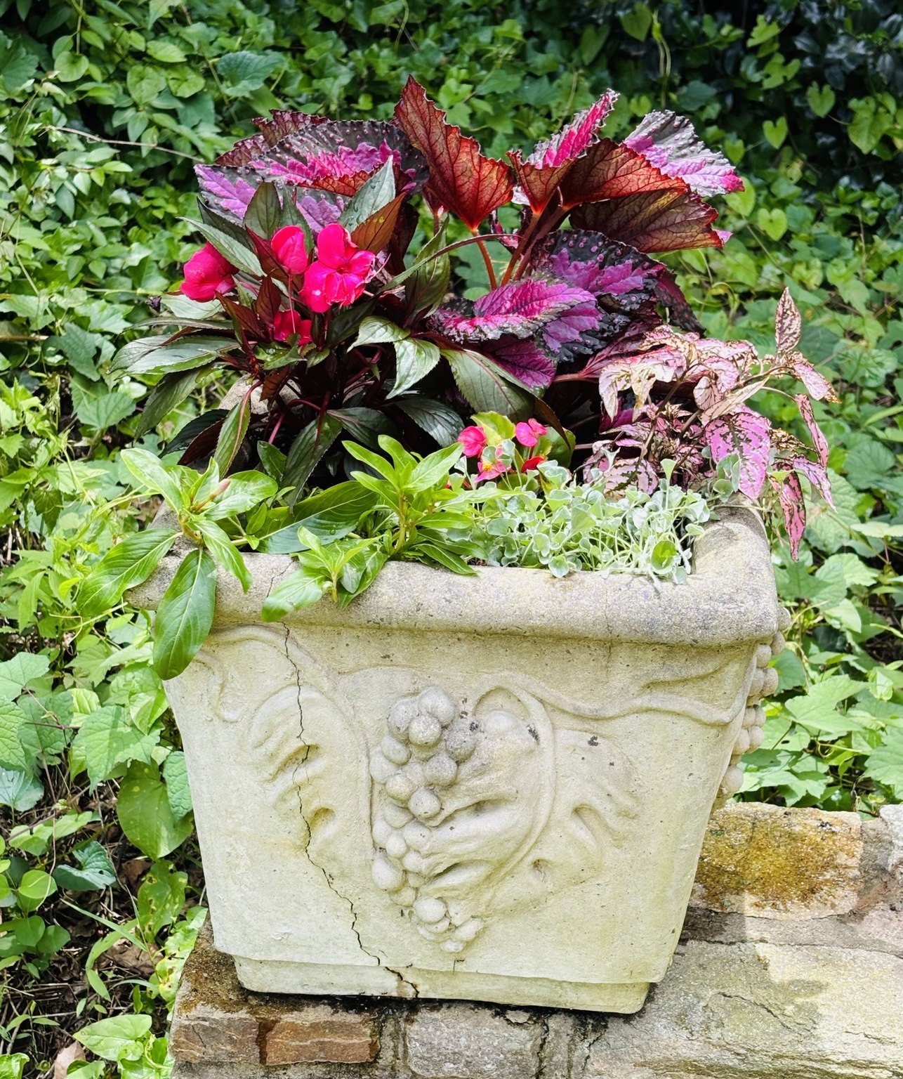 Carved pale stone planter filled with mixed foliage in a garden