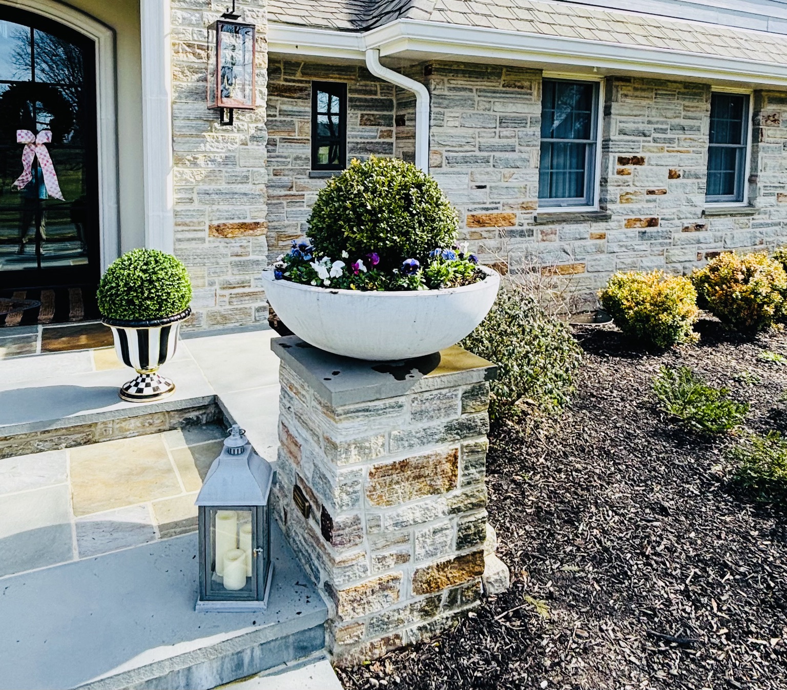 White pedestal urn with purple, white, and blue spring pansies beside a stone entry