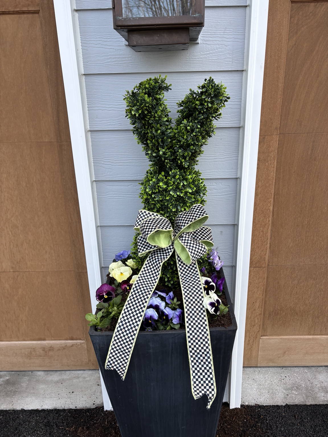Tall topiary with a black and white checkered bow above a black planter of colorful spring pansies
