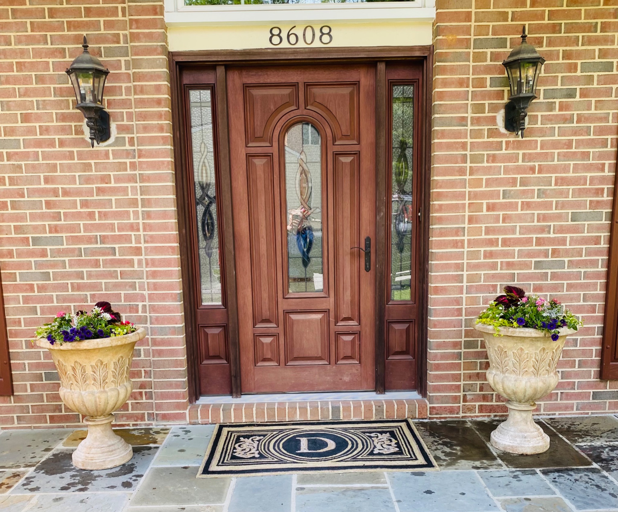 Pair of classic urns with spring flowers flanking a brick front door
