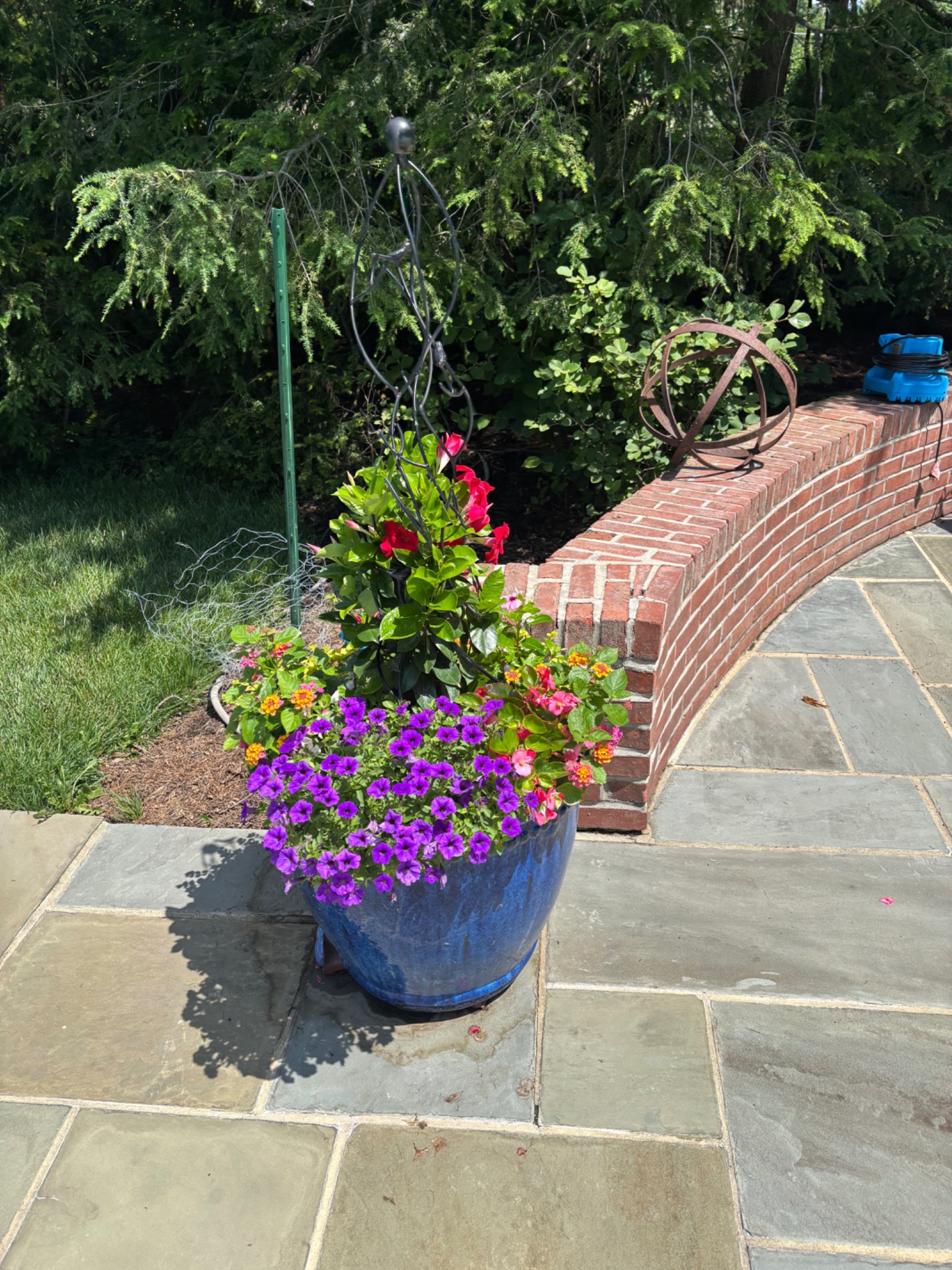 Blue glazed planter filled with pink, purple, and yellow flowers beside a brick garden wall