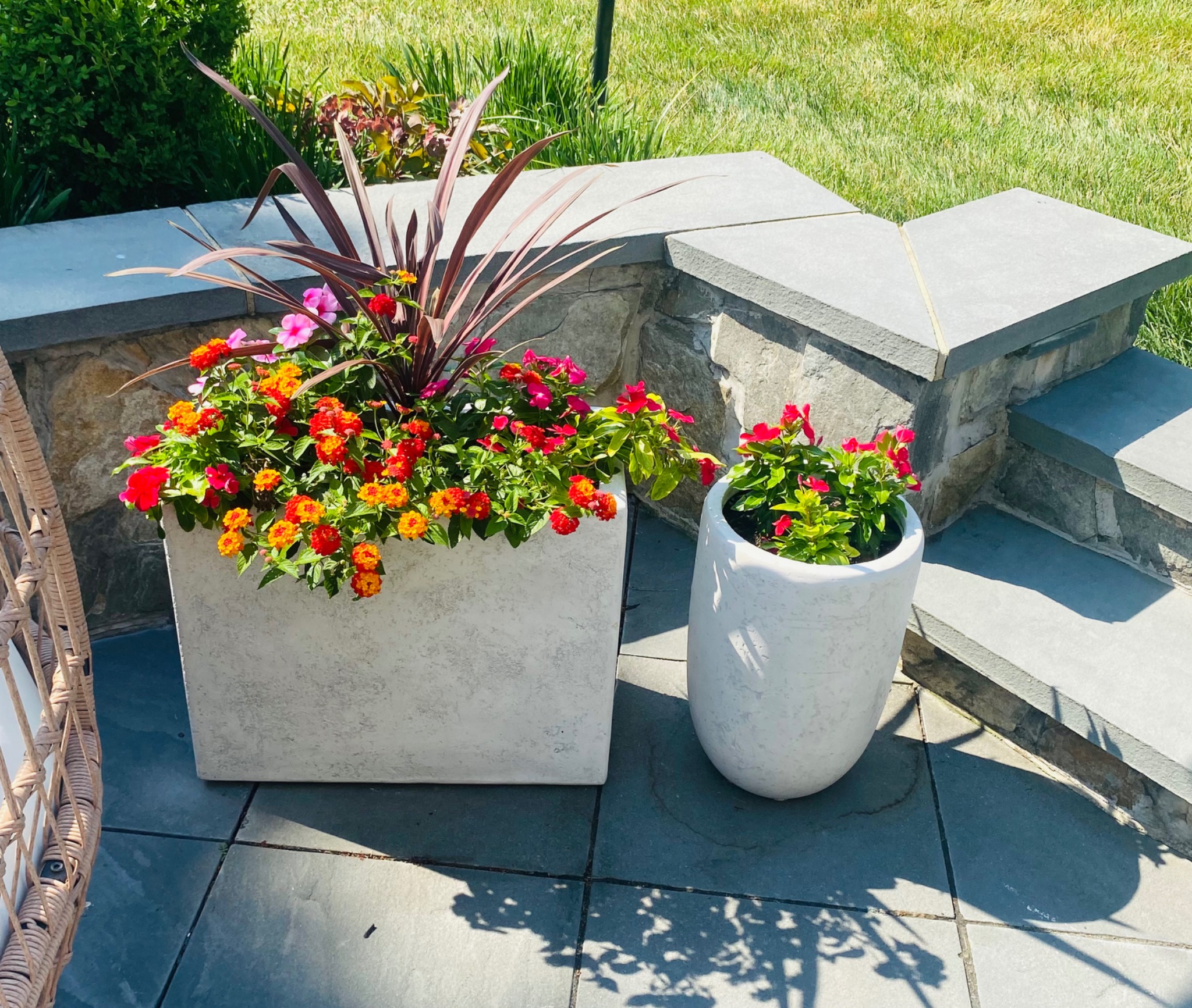Two large white planters filled with red, orange, and pink summer flowers