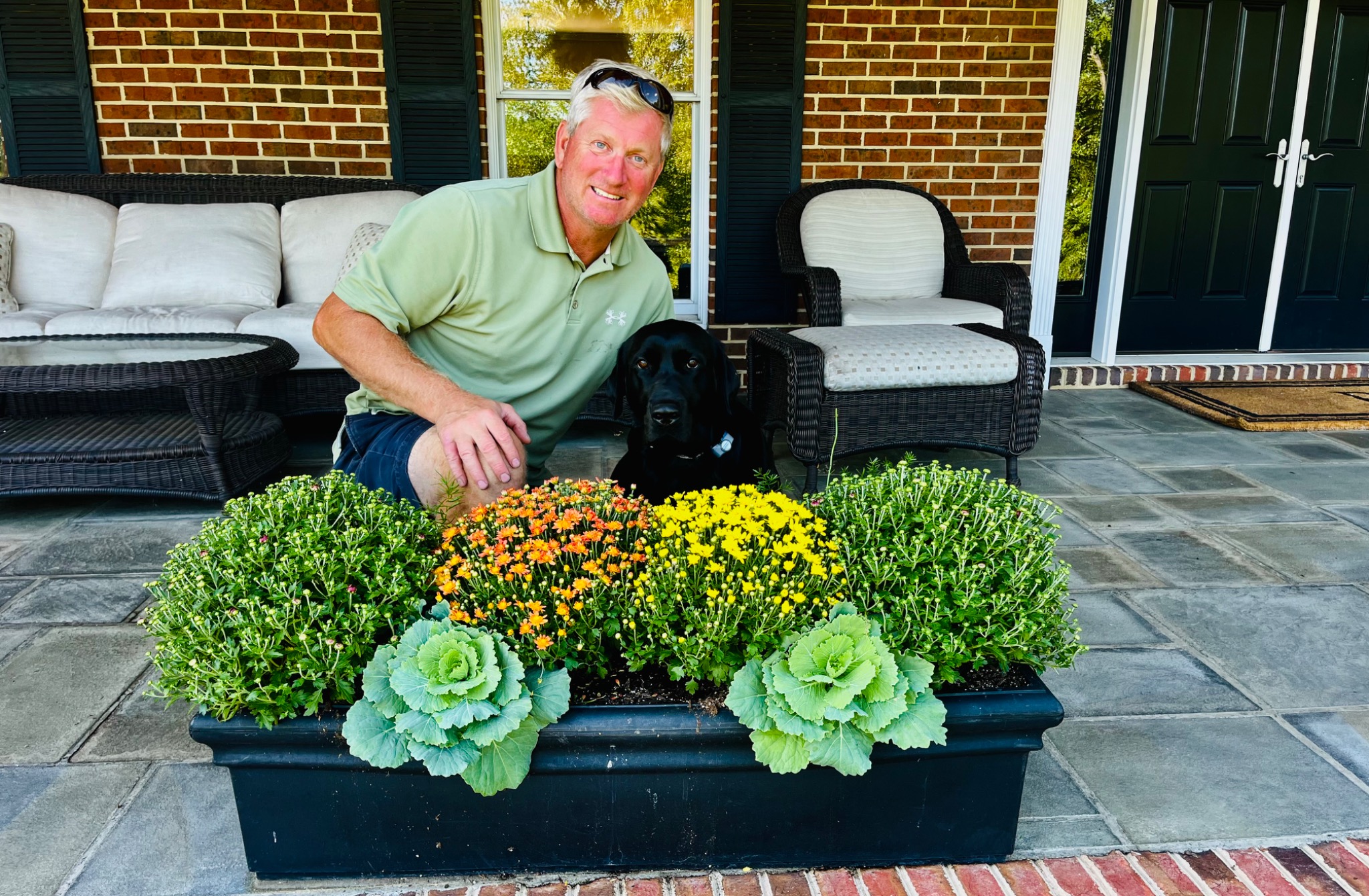Derek and his black Lab beside a fall planter with mums and ornamental kale